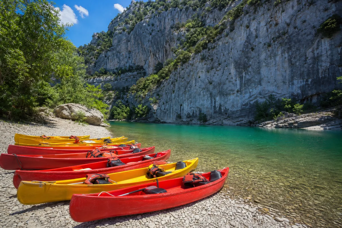 Canoës colorés alignés sur une plage de galets au bord d&rsquo;une rivière
